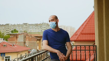 Man with protection mask on the balcony feeling down during coronavirus pandemic.