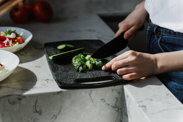 Beautiful young woman cuts a cucumber close-up.