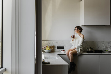 Beautiful woman in a sweater drinks coffee in the kitchen.