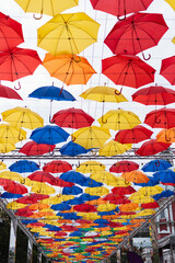 Fototapeta na wymiar Many multi-colored umbrellas in the sky, unusual summer street scenery.