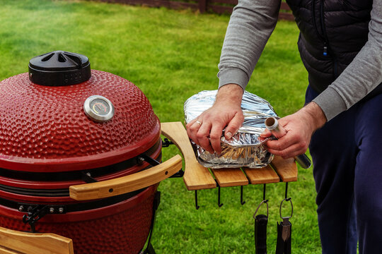 Red Ceramic Barbecue Grill. The man wraps the freshly prepared BBQ in foil.