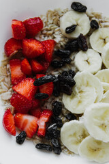 Oatmeal with strawberries, bananas and raisins close-up.
