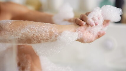 Fototapeta premium Unrecognized woman washing body with foam at bath. Woman hands touching skin