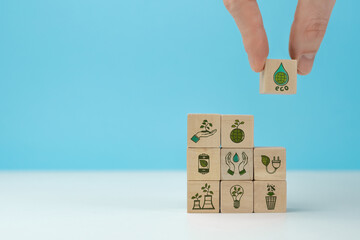 Fototapeta na wymiar Wooden blocks with environmental symbols arranged a man is holding the top one. Ecology