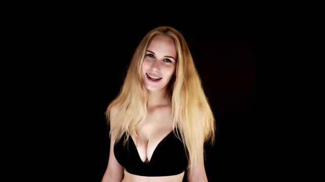 Beautiful young woman with big natural breasts in a black bra on a black background laughing at the camera.
