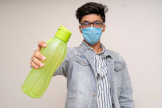 Young handsome asian boy in denims, wearing a protective mask, holding a water bottle. Confident boy showing to drink more water.