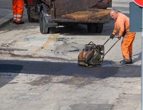 Worker regulate laying new asphalt to patch a bump in the road.