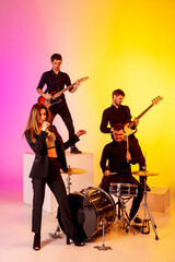 Young and joyful caucasian musicians performing on gradient studio background in neon light. Concept of music, hobby, festival. Colorful portrait of modern artist. Inspiring. Art, cover band.