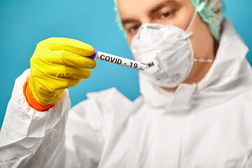 Laboratory technician wearing respirator mask and protective coverall hold medical tube for test...