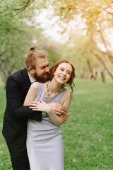 Fototapeta premium a young beautiful couple, a girl in a lilac dress and a man in black in a summer Park with Apple trees