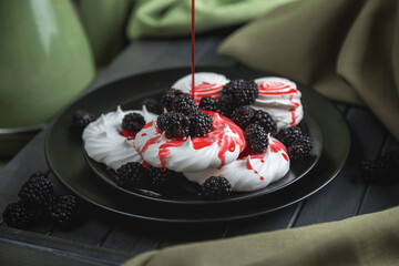 Still life, marshmallows and meringues on a black plate decorated with red berries and syrup. On a...