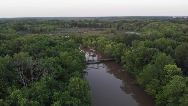 Abandoned Cox bridge above brown Kaskaskia river waters by green trees, Patoka, Illinois, aerial approach
