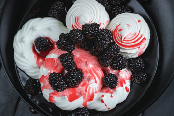 there are white sweets on black plates. Meringue and marshmallows are decorated with blueberries. White sweets are poured with red syrup. The view from the top.