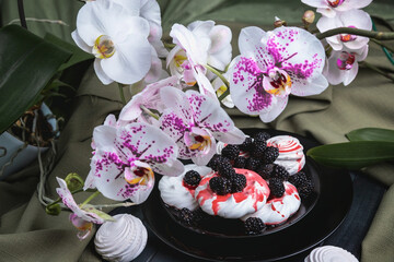 Obraz na płótnie Canvas Still life of flowers Orchid and dessert. Tender, delicious marshmallows and meringue, on a black plate.