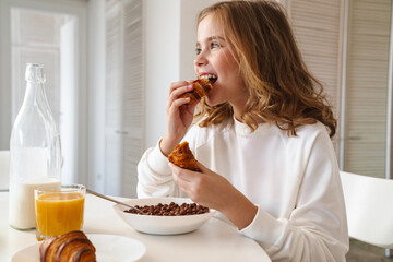 Photo of happy caucasian girl eating croissant while having breakfast