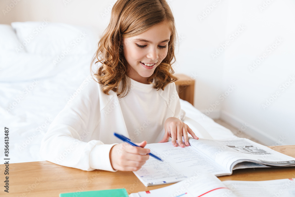 Wall mural photo of happy girl writing in exercise book while doing homework