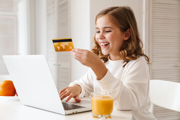 Photo of excited cute girl using laptop and holding credit card