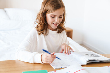 Obraz na płótnie Canvas Photo of happy girl writing in exercise book while doing homework