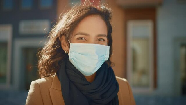 Portrait of a Beautiful Dark Haired Young Woman Wearing Protective Medical Face Mask and Standing on the Street. Safe and Happy Woman Practicing Social Distancing, Quarantine. Blurred City Background