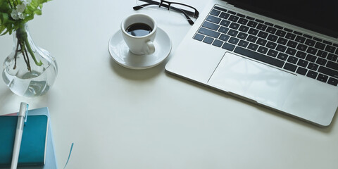 The top view image of the white working desk is surrounding by a coffee cup and office equipment.