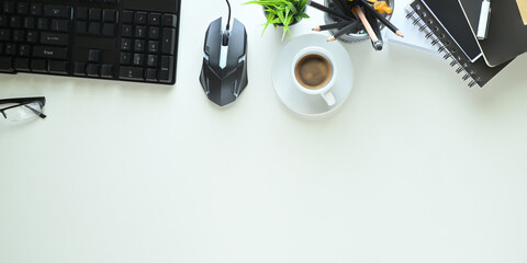 The top view image of the white working desk is surrounding by a coffee cup and office equipment.