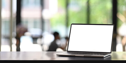 Computer laptop is putting on a counter bar over people in co working space as a background.