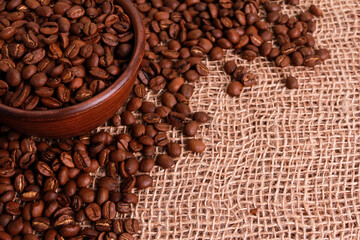 Coffee beans in clay bowl on jute burlap sackcloth surface. Closeup, copy space, high angle. Arabica seeds, traditional roast concept