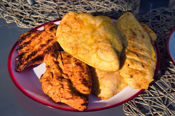 grilled food such as grilled chicken brest and chicken sticks lying on a red and white plate that...