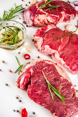Raw meat, beef steak on cutting board with rosemary and spices, white background, top view copy space