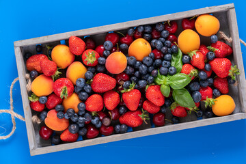 strawberries, blueberries, cherries and peaches in a wooden box.