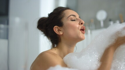 Closeup hot woman blowing foam at bathtub. Sexy girl playing with bubbles
