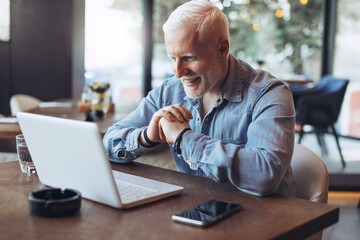 Mature businessman working on laptop. Mid adult entrepreneur working on laptop at restaurant. Confident and smiling businessman working on laptop at restaurant.