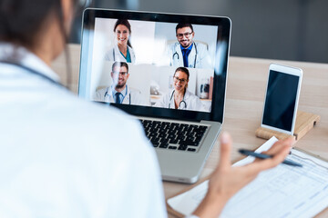 Female doctor talking with colleagues through a video call with a laptop in the consultation.