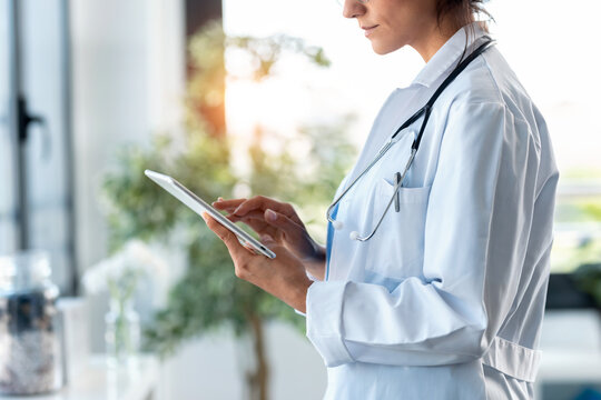 Beautiful female doctor using her digital tablet while standing in the consultation.