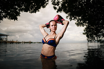 Beautiful woman in black boxing glows and topples naked posing at the Caribbean sea on the beach