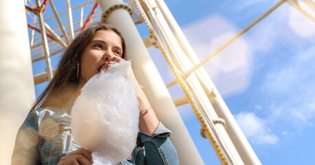 joyful brunette in jacket eats cotton candy of white colour