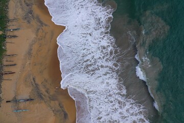 aerial drone bird view shot of the sea shore with turquoise water, an empty yellow sand beach with fishing long boats, white waves and foam forming beautiful textures, patterns, shapes. Sri Lanka