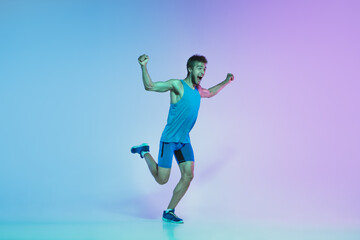 Fototapeta na wymiar The first. Portrait of young caucasian man running, jogging on gradient studio background in neon light. Professional sportsman training in action and motion. Sport, wellness, activity, vitality