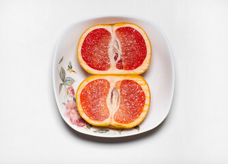 Naklejka na ściany i meble photo of the inside of two halves of the same pink grapefruit lying in a light plate on a light background.