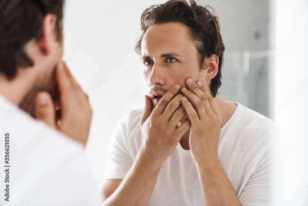 Wall mural attractive young man standing in front of the bathroom mirror