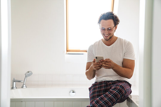 Smiling young man wearing pajamas sitting on a bathtub