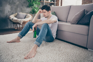 Portrait of his he nice attractive addicted depressed guy sitting on carpet drinking beer feeling...