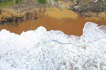 aerial drone bird view shot of the sea shore with yellow sand, black rocks, large white waves and foam crashing on the beach forming beautiful textures, patterns, shapes. Sri Lanka