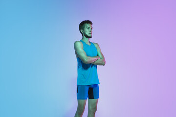 Fototapeta na wymiar Resting. Portrait of young caucasian man running, jogging on gradient studio background in neon light. Professional sportsman training in action and motion. Sport, wellness, activity, vitality concept