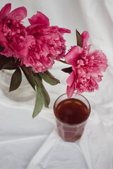 glass with tea and a bouquet of flowers on a white vintage background. flowers red peonies
