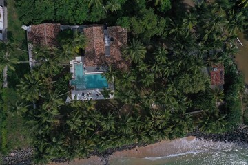 aerial drone bird view shot of the sea shore with turquoise blue water, a villa with a beautiful garden with swimming pool, green palm trees and tropical vegetation. Polhena, Sri Lanka