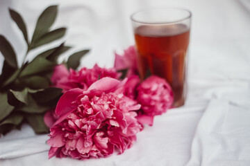 Obraz na płótnie Canvas glass with tea and a bouquet of flowers on a white vintage background. flowers red peonies