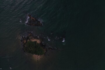 aerial drone bird view shot of the sea surface with turquoise blue water, a small island, brown black rocks and stones, white waves and foam forming beautiful textures, patterns, shapes. Sri Lanka