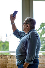 Fototapeta premium Keep your memories in your phone. Senior man taking a self picture. Close up. Focus on background. Senior man making selfie with smart phone.
