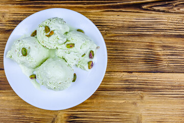 Glass bowl with pistachio ice cream balls and nuts on a wooden table. Top view
